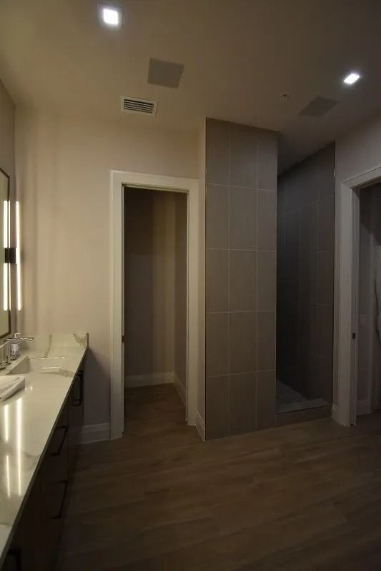 Bathroom with a long countertop, walk-in shower, and wooden floor; neutral color scheme.