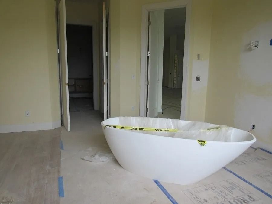 White bathtub in a light yellow room under construction. Two open doorways lead to other rooms.