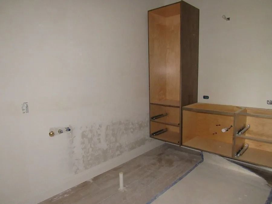 Kitchen under construction with bare cabinets and plumbing against a light wall.
