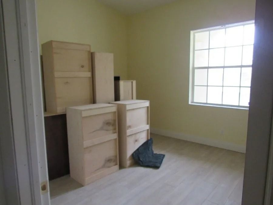 Empty room with light-colored walls and flooring; several wooden boxes are stacked inside, near a window.