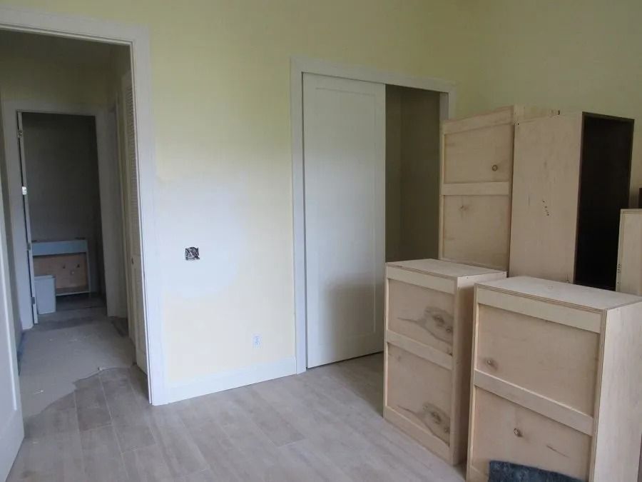Room with unfinished cabinets, a doorway to a bathroom, and a sliding closet door. Light yellow walls and wood floors.