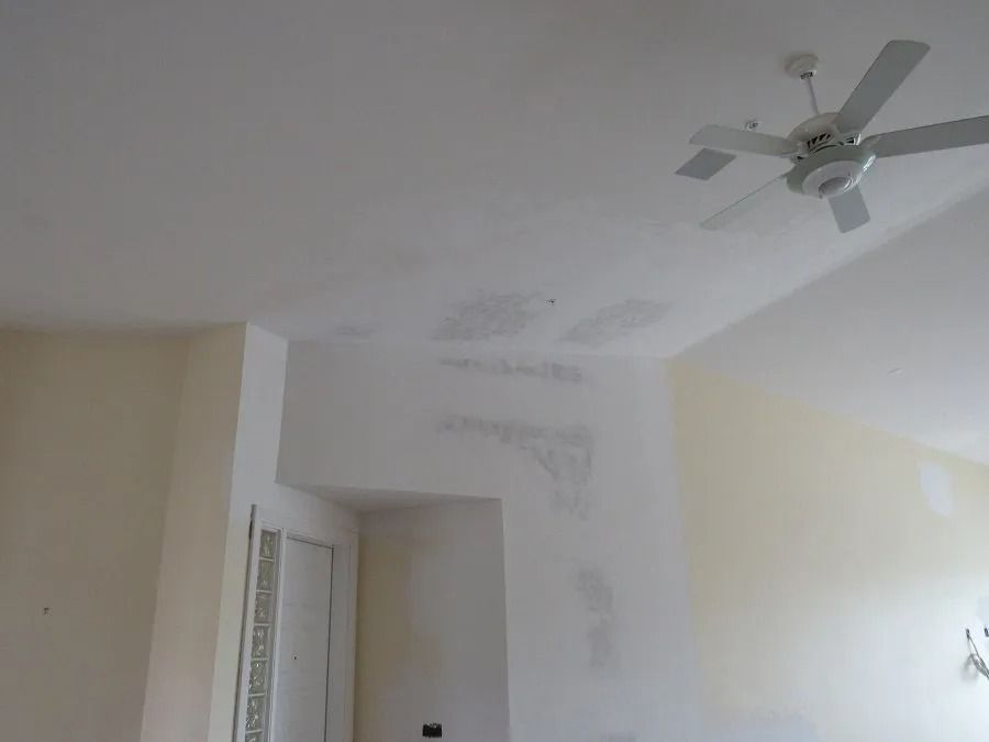 White room interior with peeling ceiling paint, fan, and doorways.