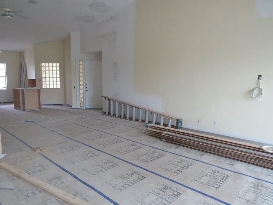 Interior of a room under construction with exposed flooring, ladder, and raw materials. Walls are painted cream.