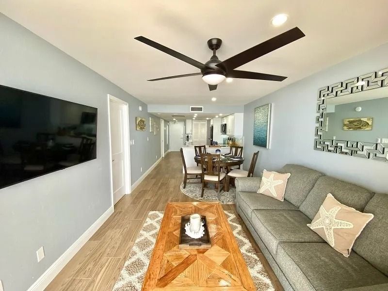 Living room with TV, couch, dining table, and ceiling fan in a light blue-walled space.