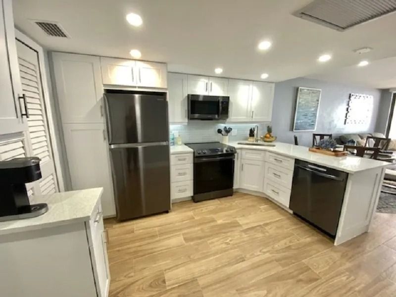 Modern white kitchen with stainless steel appliances and light wood floors.