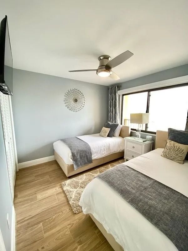Bedroom with two twin beds, pale blue walls, wooden floor, and a window.