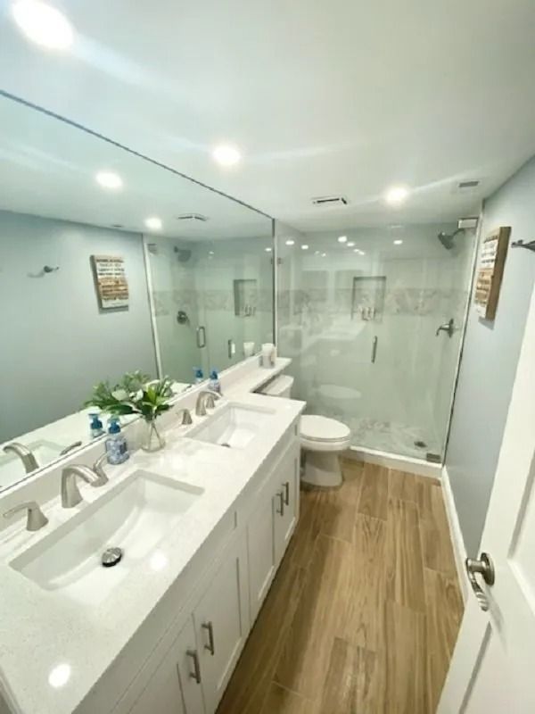 Bright bathroom with white vanity, double sinks, glass shower, and light wood-look floors.