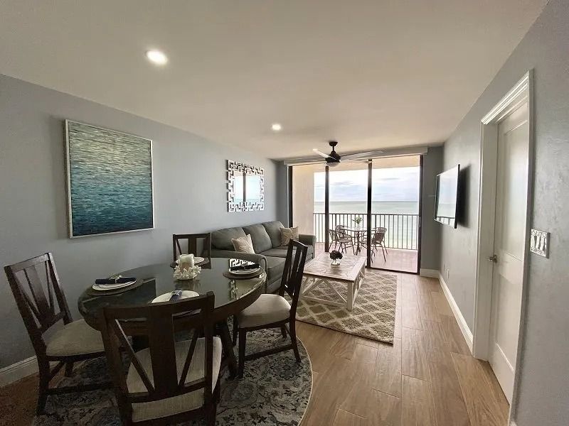 Living room with ocean view, dining table, sofa, art, and sliding glass door to balcony.