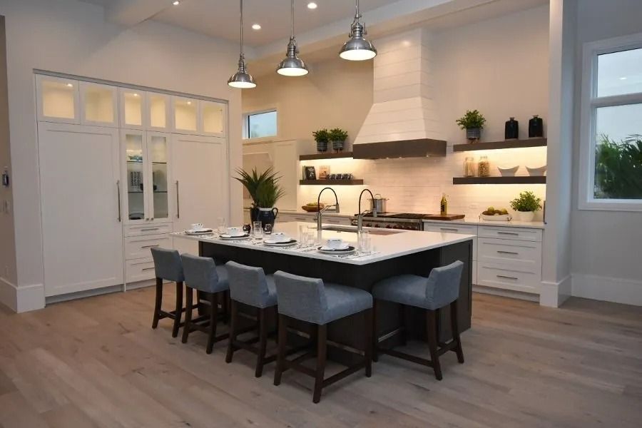 Modern kitchen with island, white cabinets, wood floors, and stainless steel pendant lights.