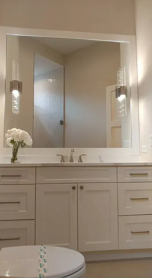 White bathroom vanity with large mirror, sconces, and flower arrangement.
