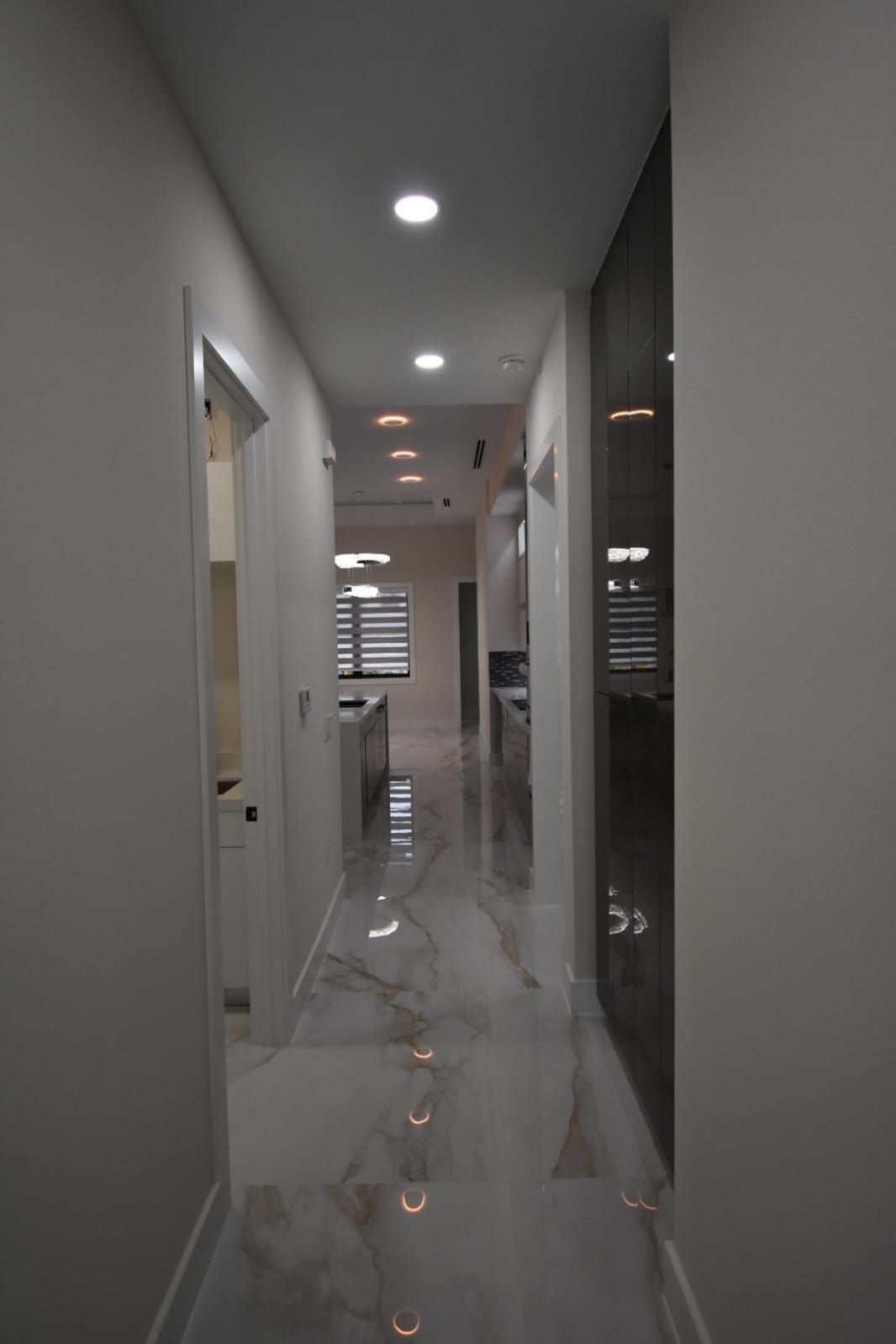 Narrow hallway with marble floor, recessed lights, and door on the left.