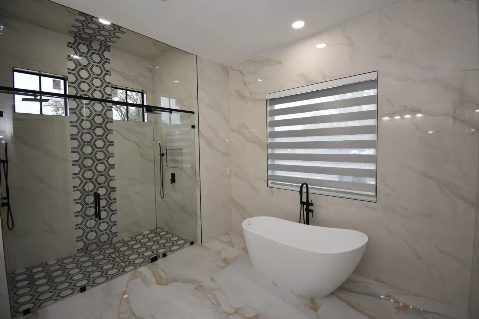 Modern bathroom with a white tub, glass shower, and patterned tile accent.