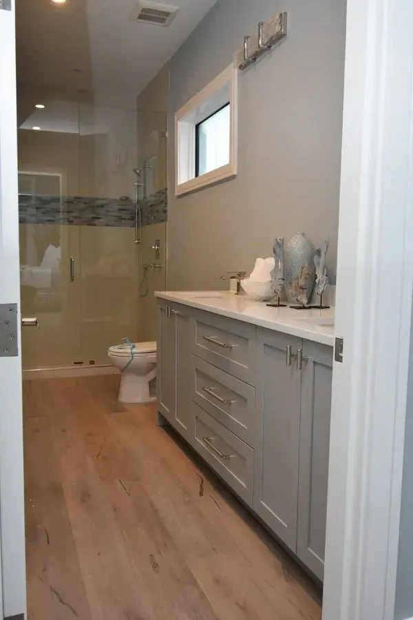 Bathroom with gray vanity, white countertop, shower, toilet, and light wood flooring.