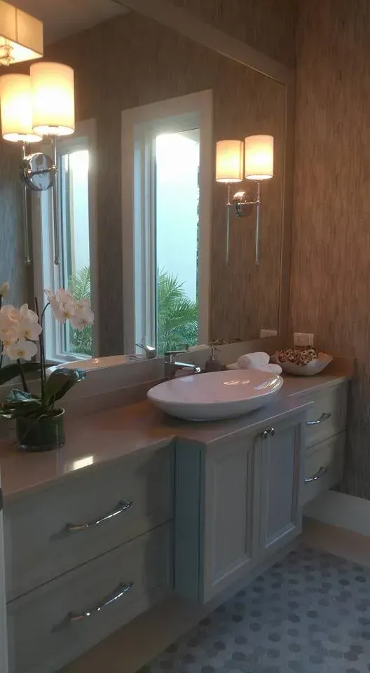 Bathroom with a vessel sink, large mirror, sconces, and neutral-toned cabinets against textured wallpaper.