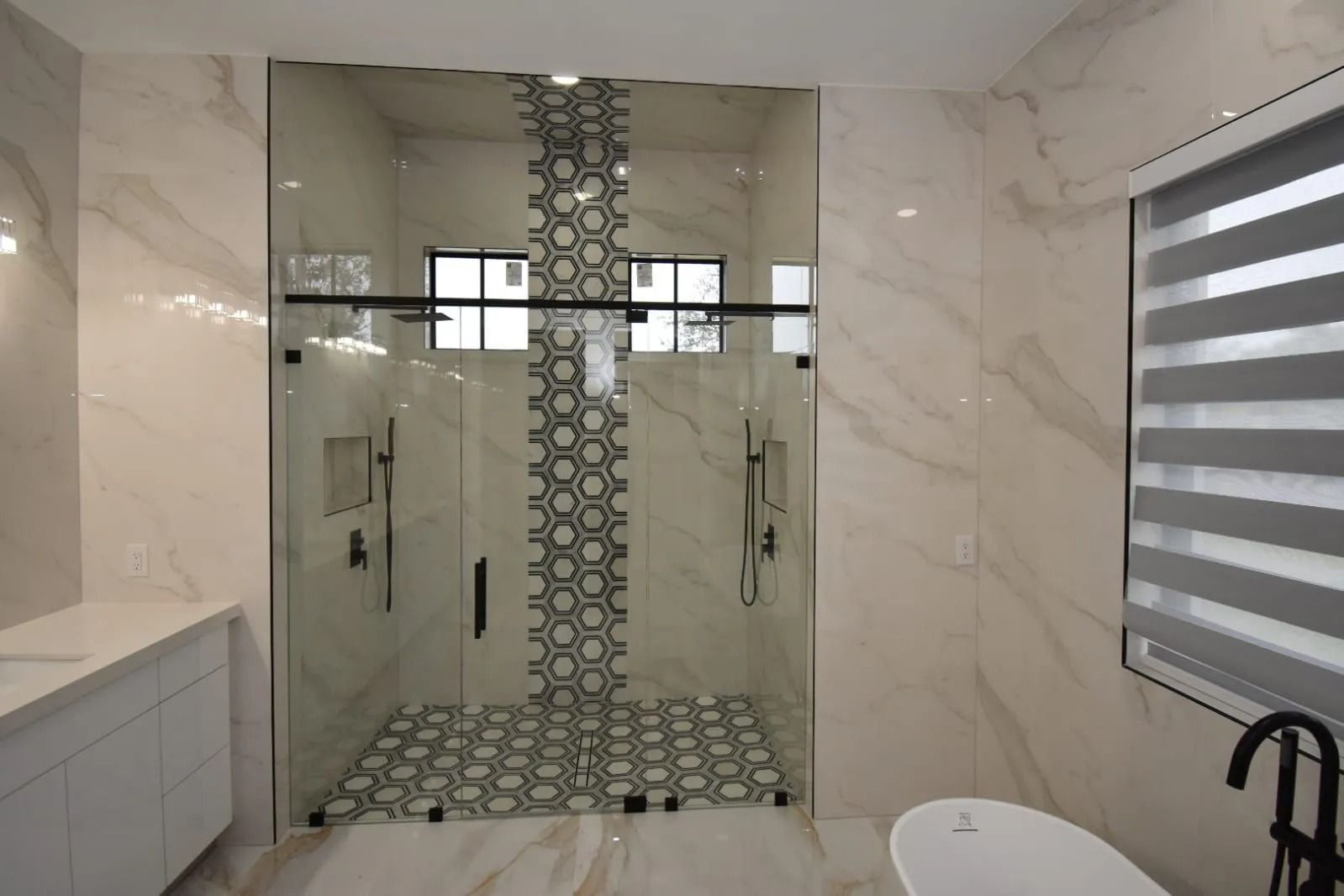 Modern bathroom with glass shower, mosaic accent, marble walls, and blinds.