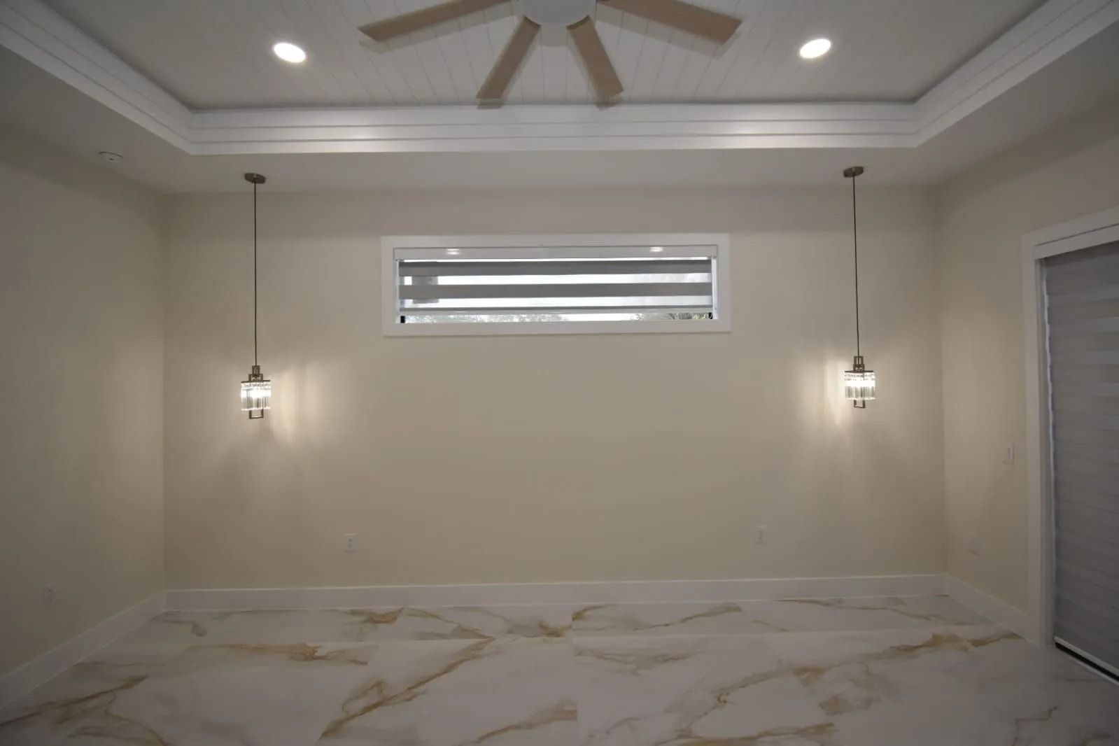 Empty beige bedroom with marble floor, pendant lights, a window, and a ceiling fan.