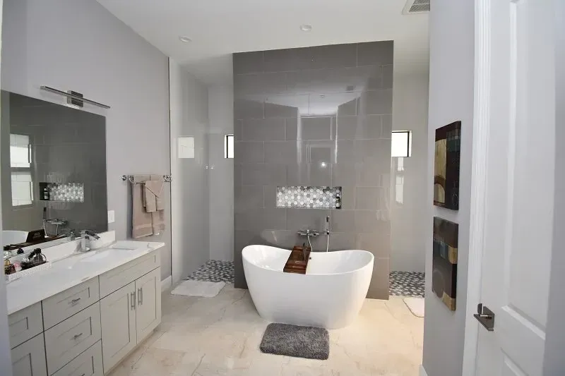 Modern bathroom with gray walls, white freestanding tub, and a large mirror.