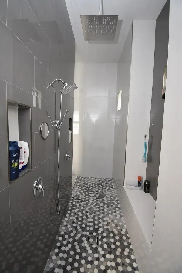 Modern bathroom with gray and white tile, pebble floor, built-in shelf, and rain shower.