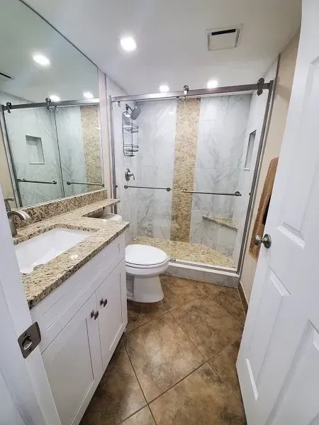Bathroom with white vanity, toilet, and shower with stone accents and a glass sliding door.