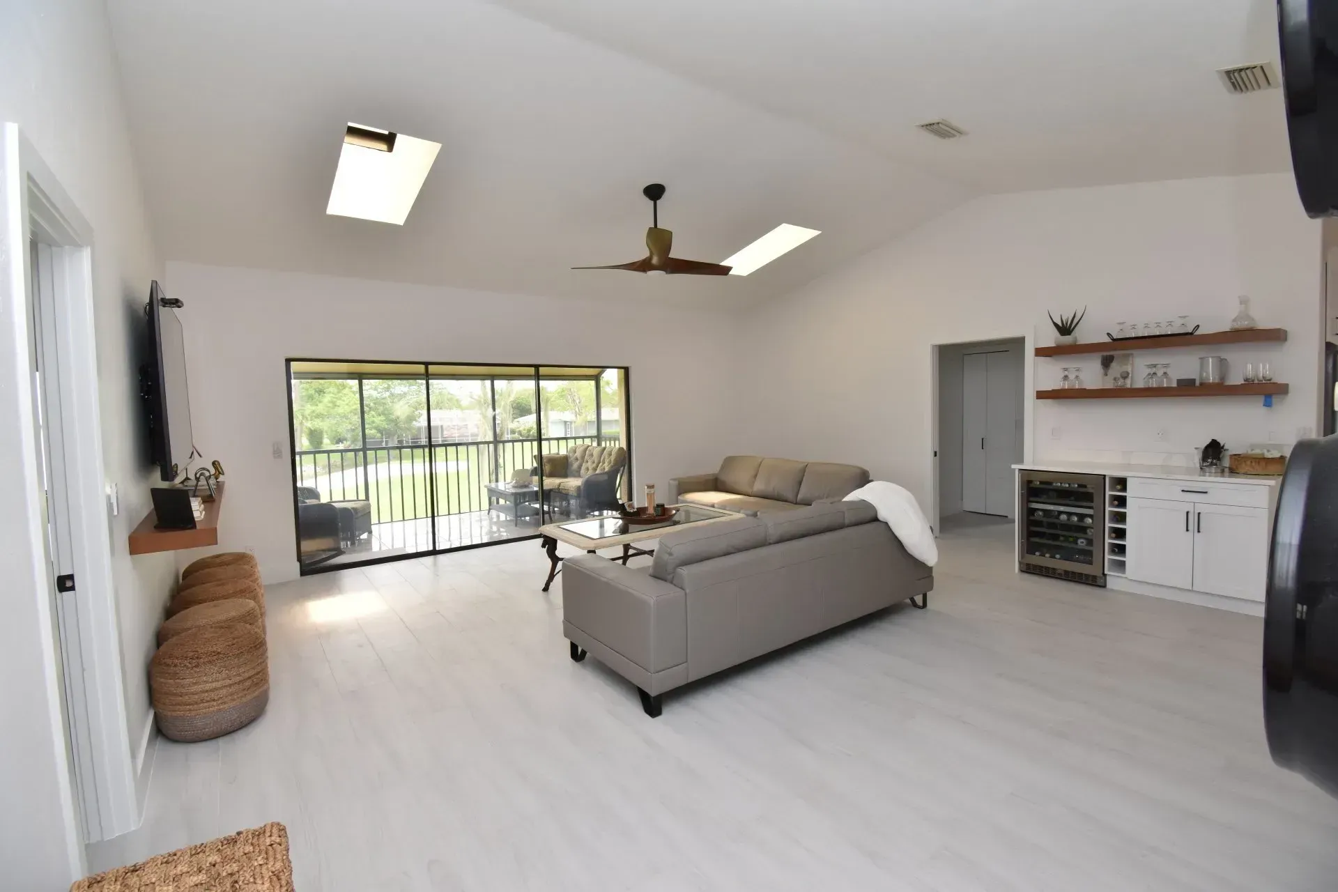 Bright, open living room with skylights, light gray couch, and sliding door to a balcony.
