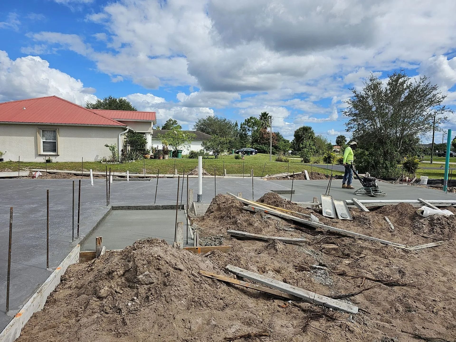 Construction site with freshly poured concrete foundation; worker using a power tool.