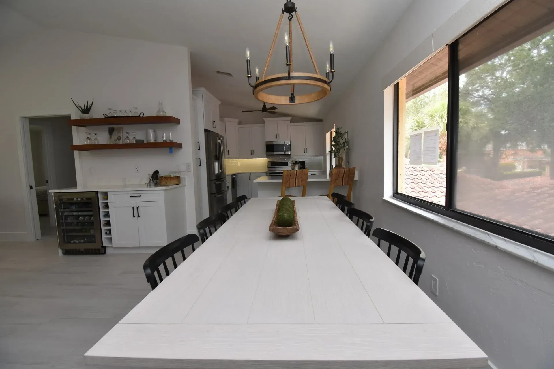 Long dining table in a bright room with a chandelier and a view through a large window.