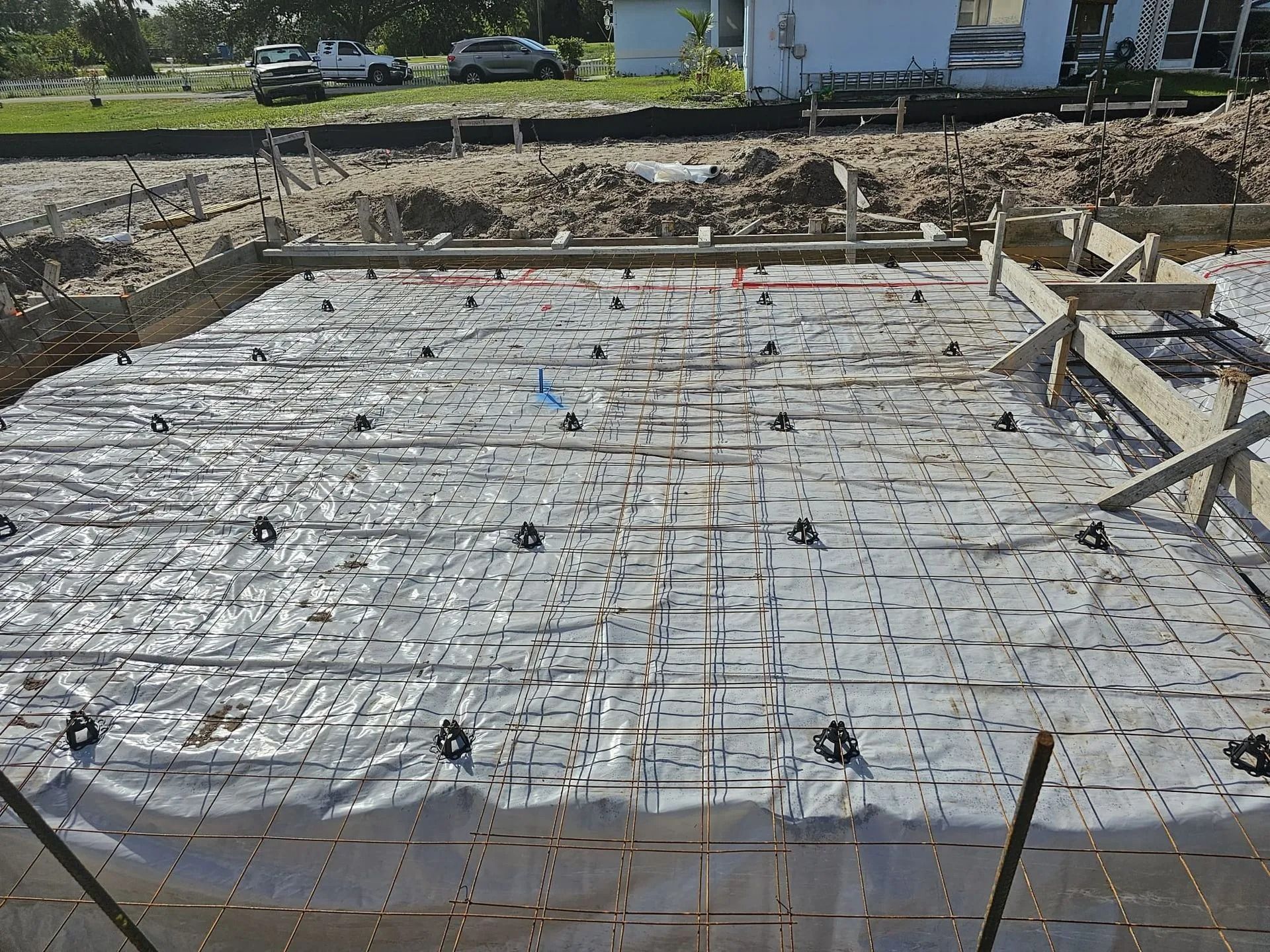 Construction site: concrete foundation form with rebar, plastic sheeting, and black supports.