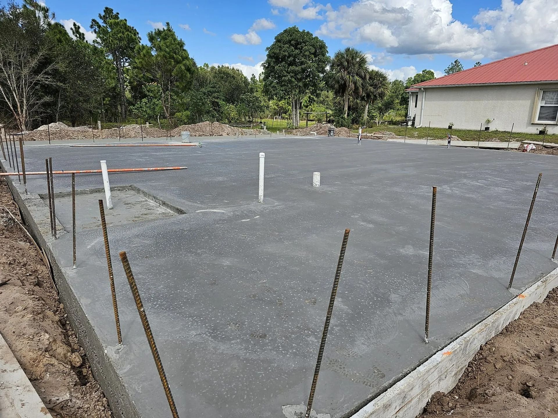 Concrete slab with exposed rebar and plumbing, outdoors.