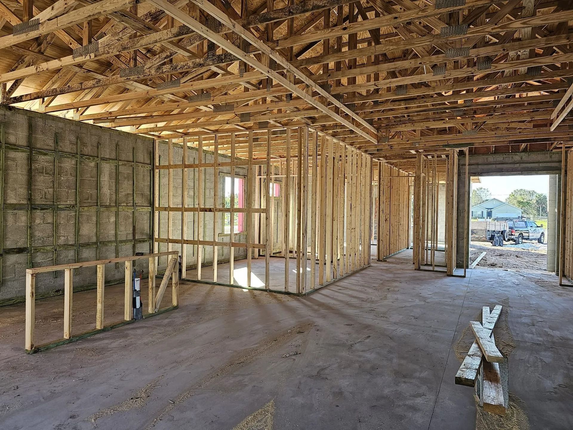 Interior view of a building under construction with wooden framing, concrete floor, and insulation on the walls.