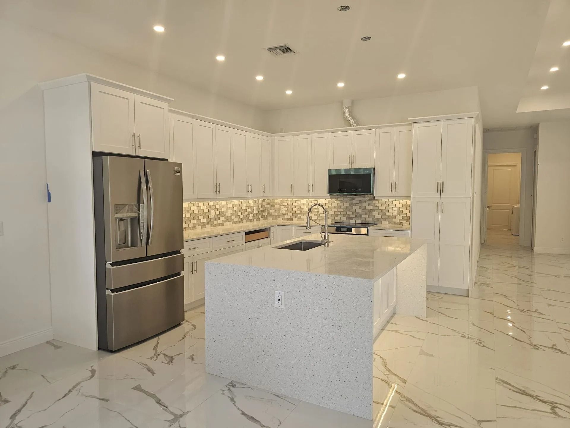 Modern white kitchen with stainless steel appliances and large island.