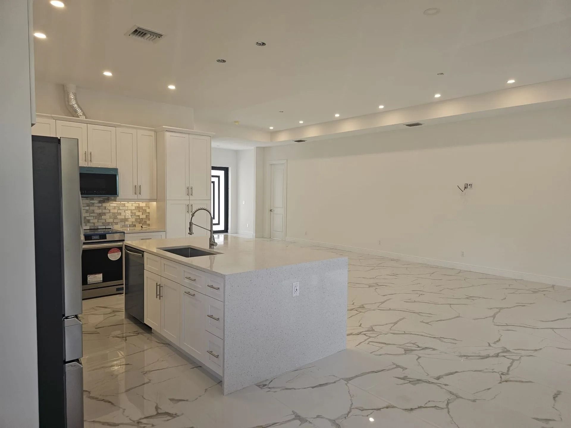 Modern kitchen with white cabinets, marble floors, and a large island.