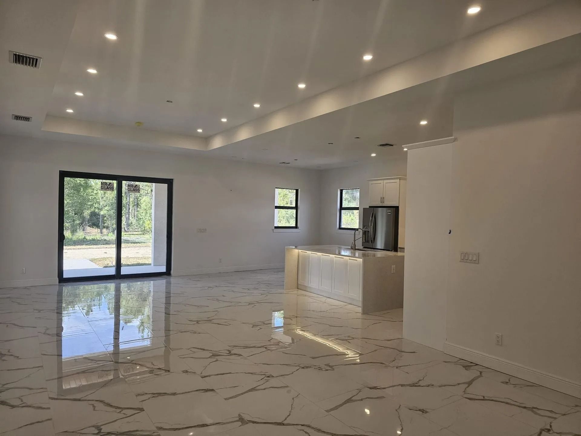 Spacious, empty interior with marble floors, white walls, recessed lighting, and glass sliding doors.