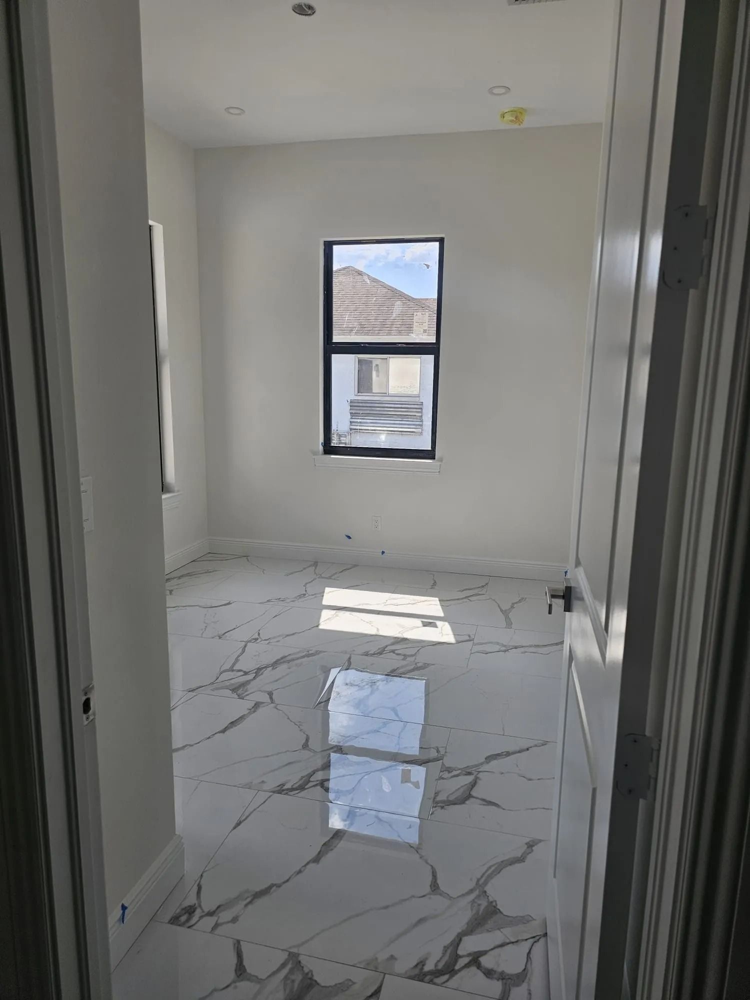 Empty room with marble-like floors, a central window, and sunlight streaming in.