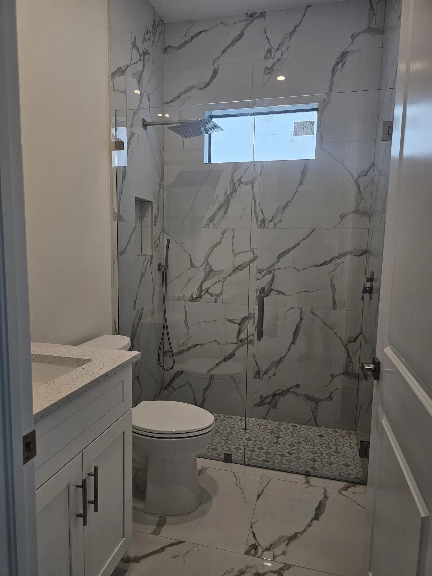 Bathroom with marble tile shower, glass doors, white vanity, and toilet.