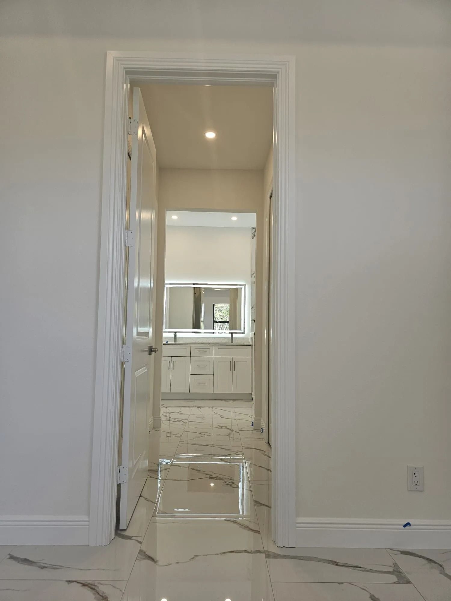 Doorway leading into a white bathroom with marble floors, vanity, and mirror.