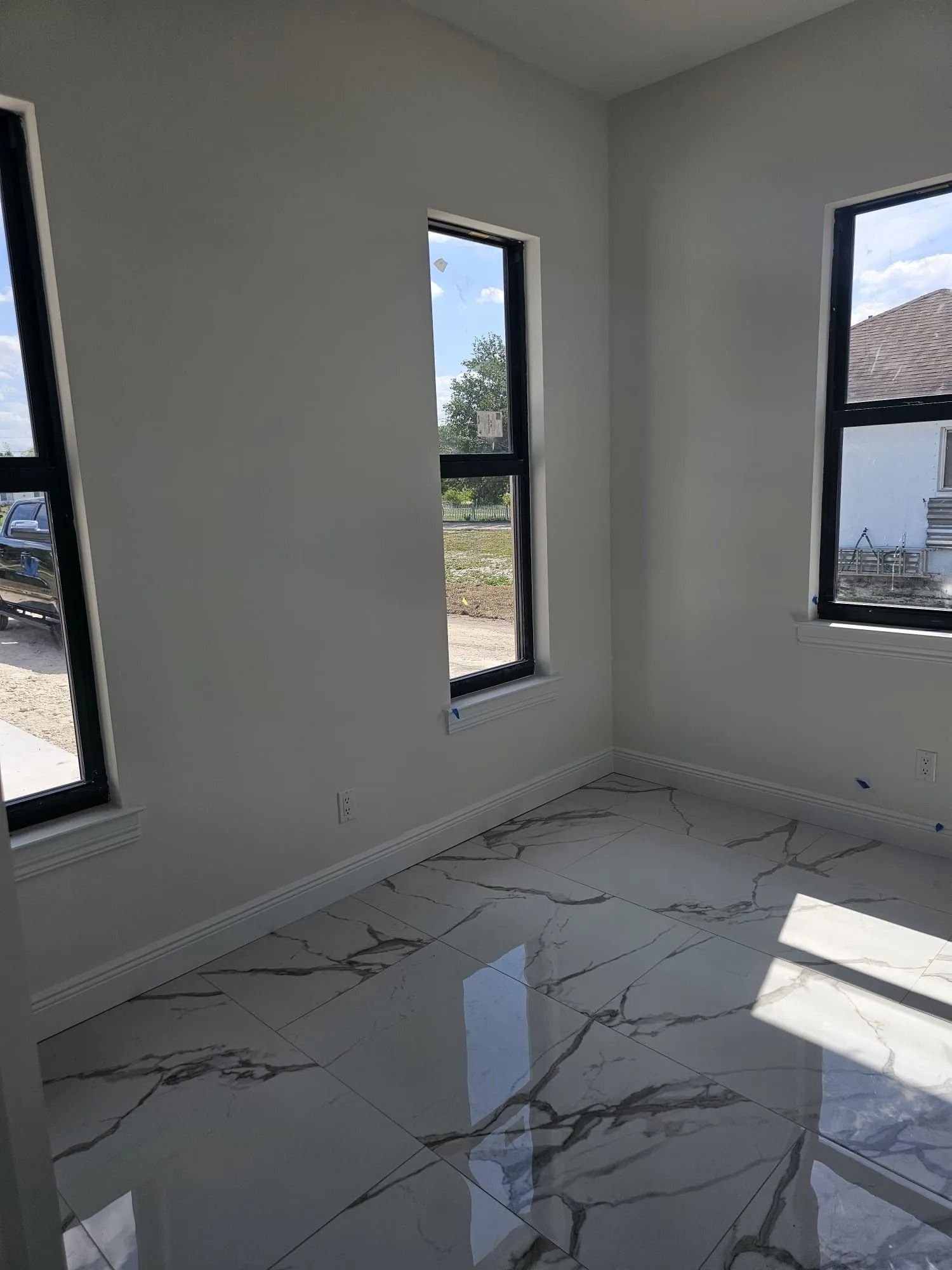 Empty room with white walls, marble floors, and three tall windows with black frames.