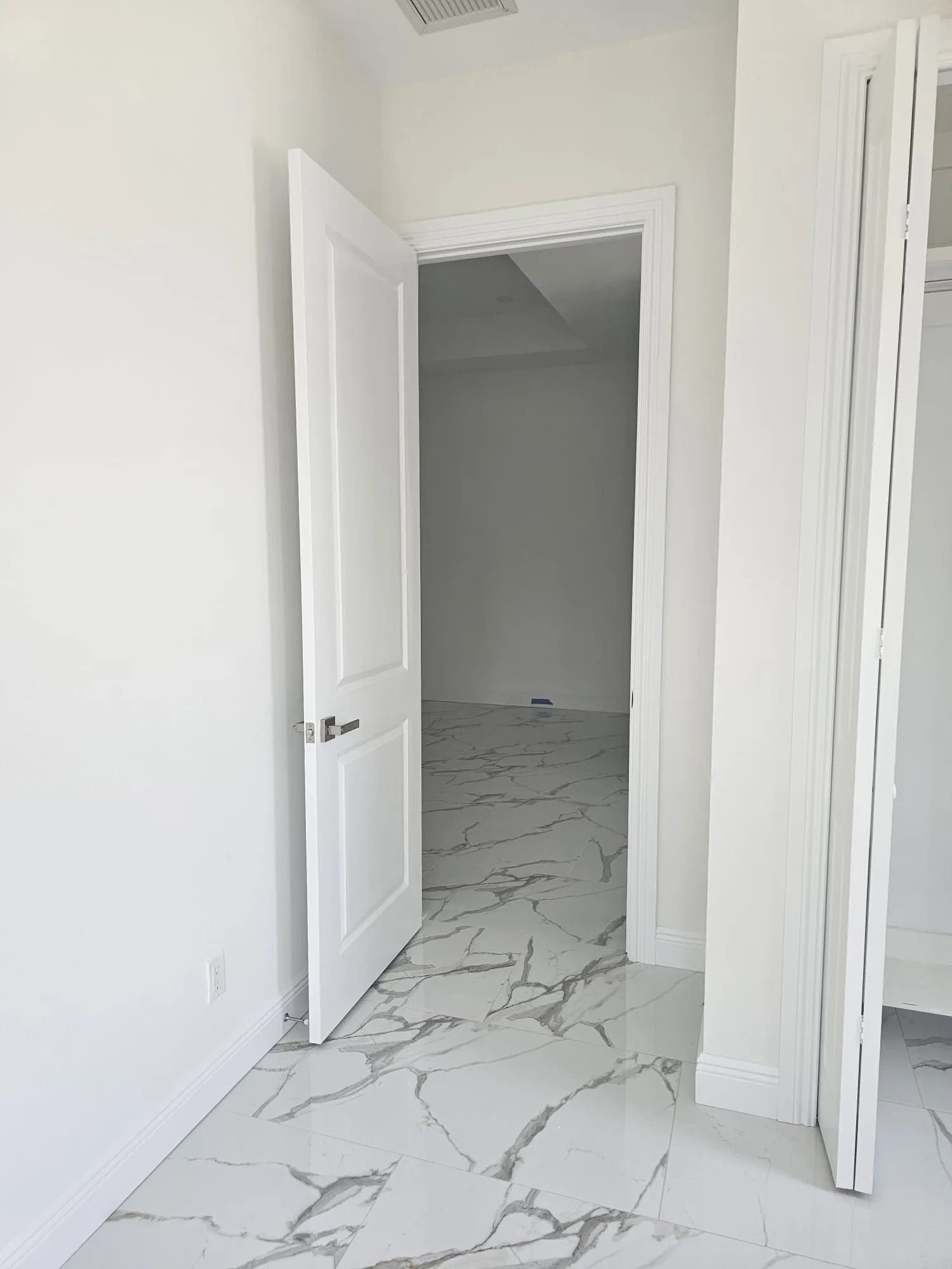 White door opens to a bright room with marble-look floors.