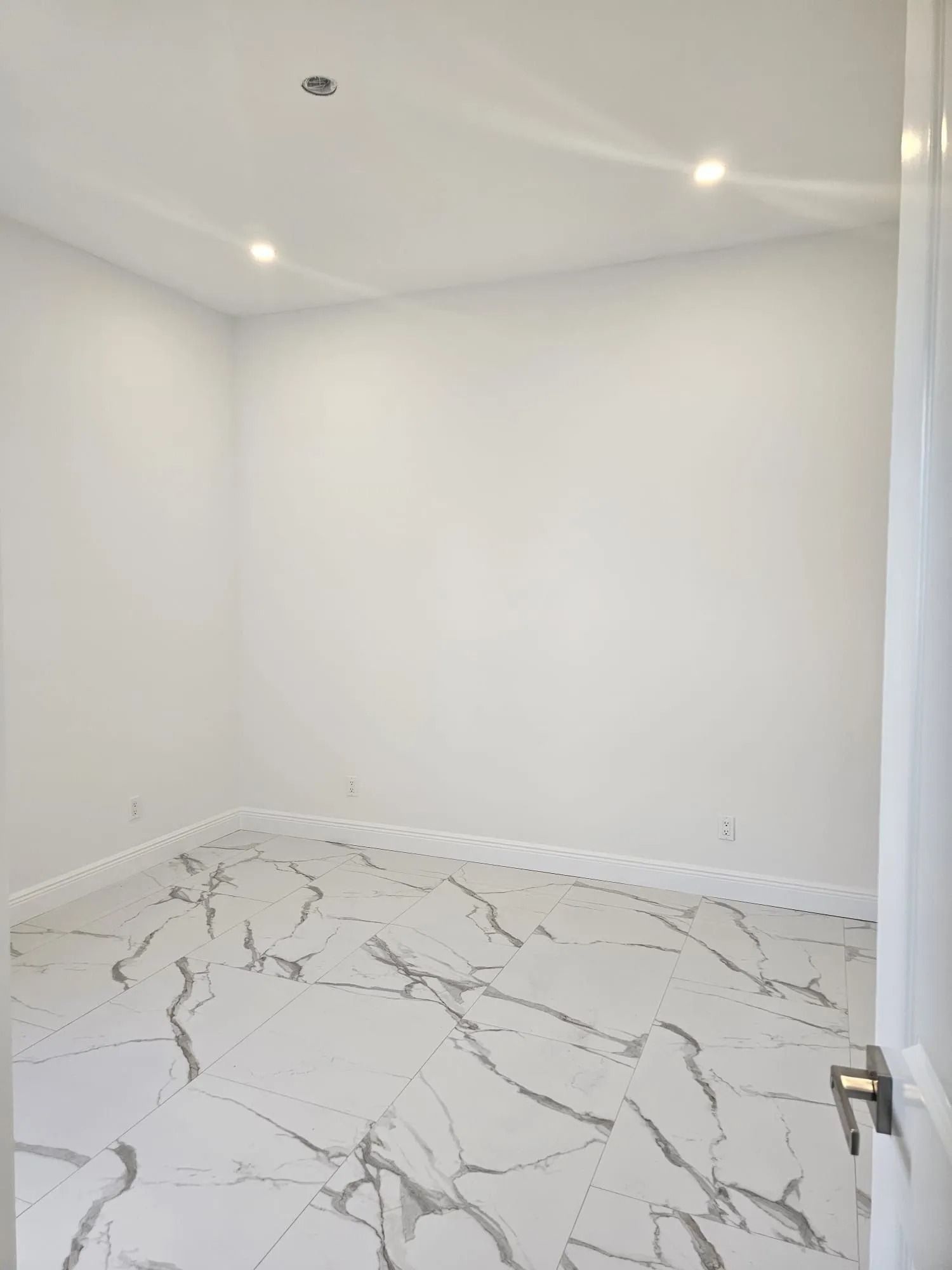 Empty white room with marble flooring and recessed ceiling lights.