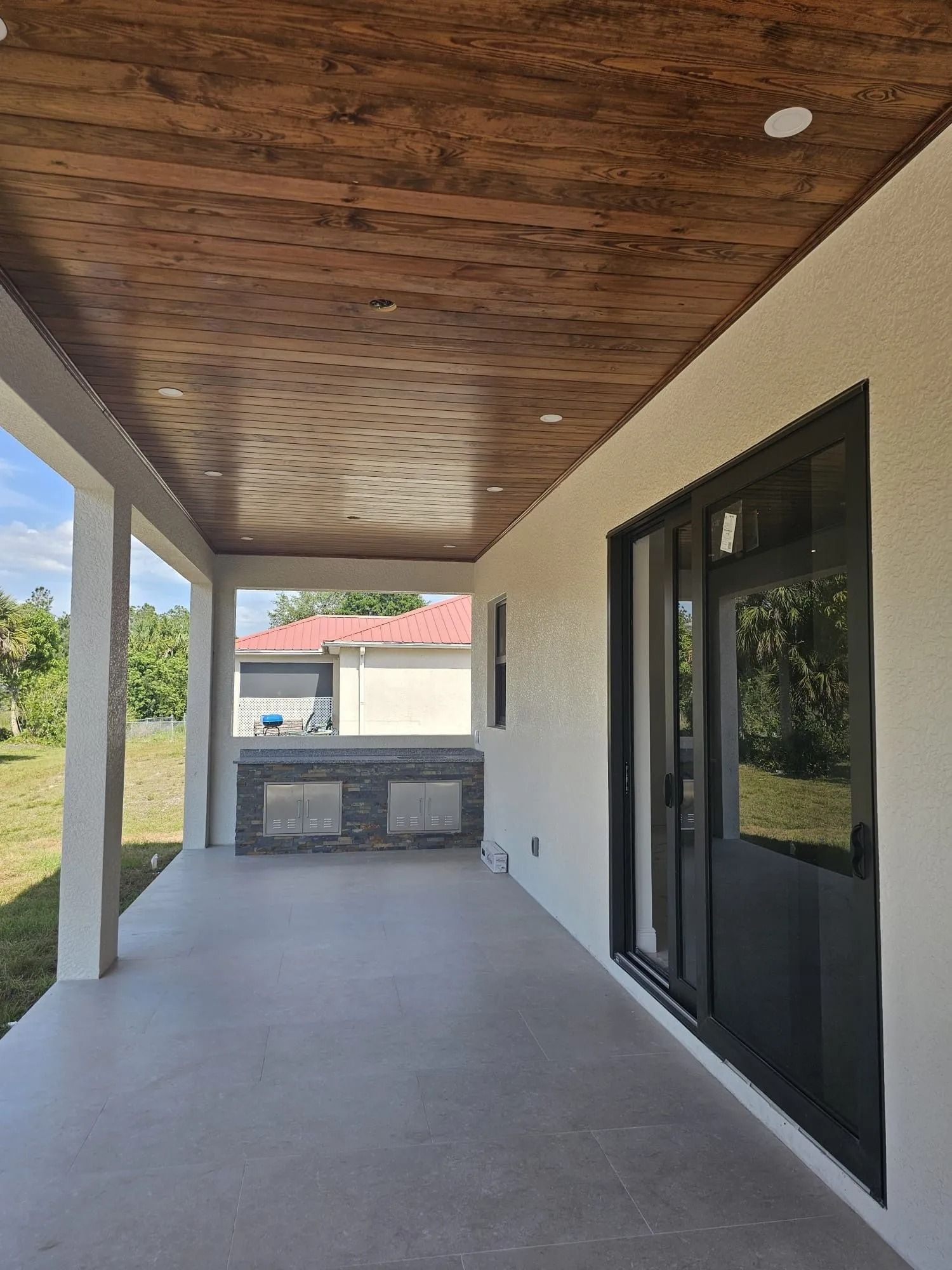 Covered patio with wood ceiling, recessed lights, and black-framed glass doors. White walls and columns.