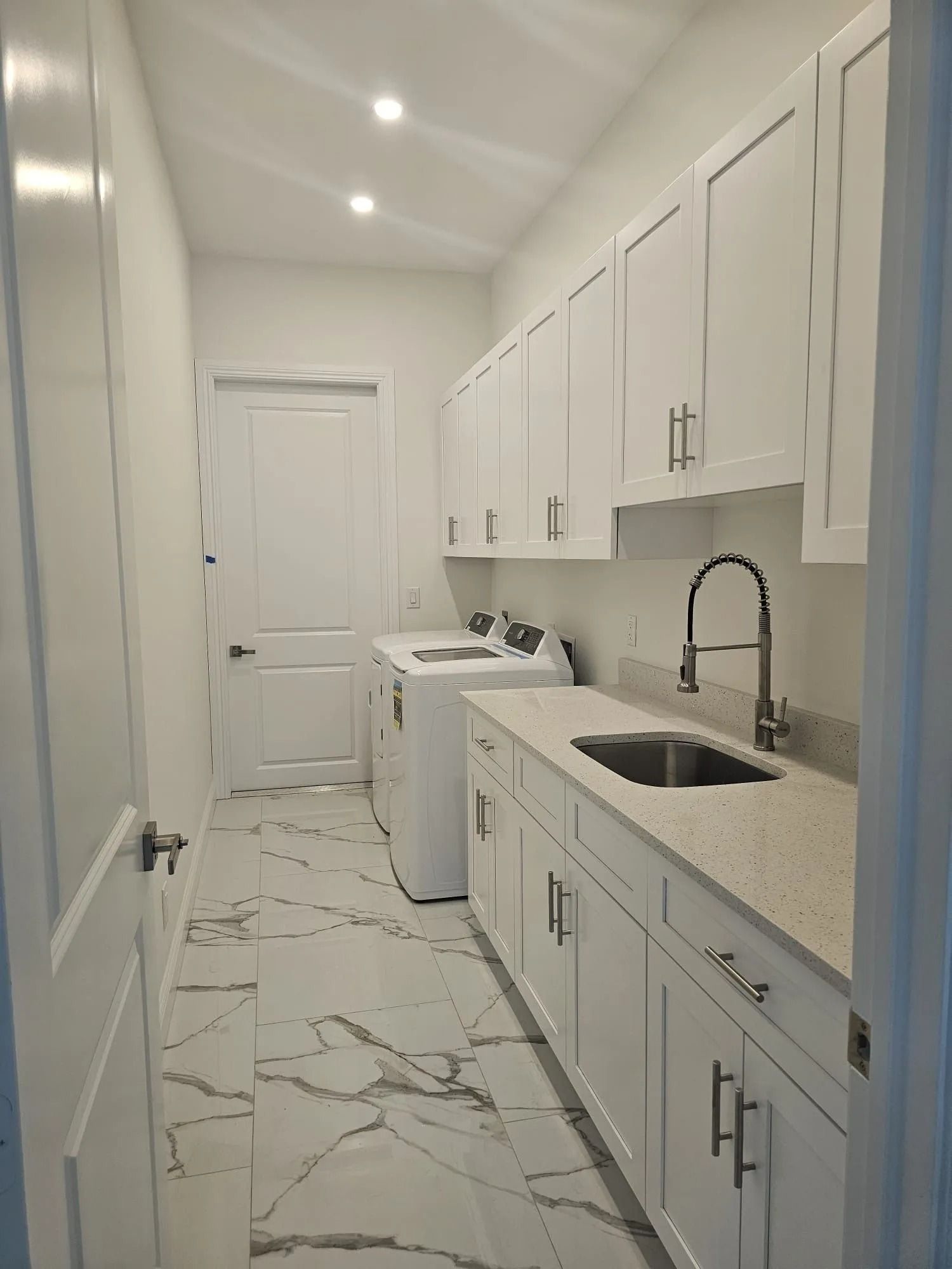 White laundry room with cabinets, sink, and washing machine; marble floor.
