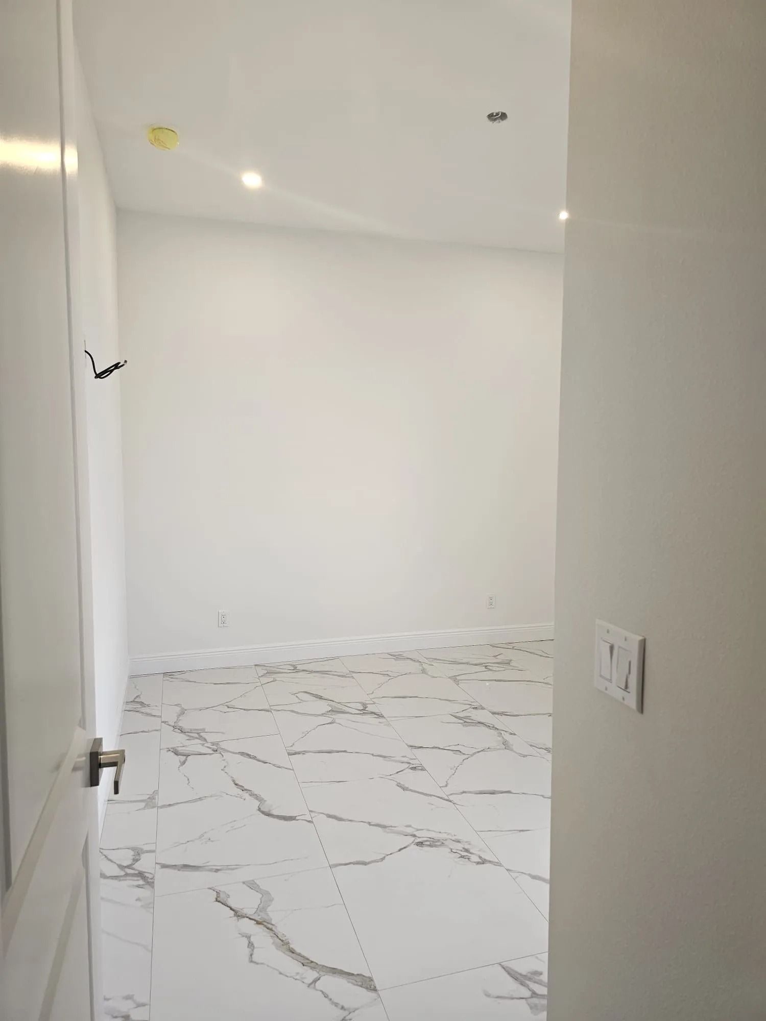 White room with marble-like floor, seen through a doorway; light switch on right wall.