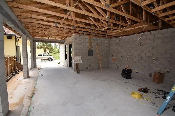 Construction site: concrete floor, cinder block walls, exposed wooden ceiling, open garage-like structure.
