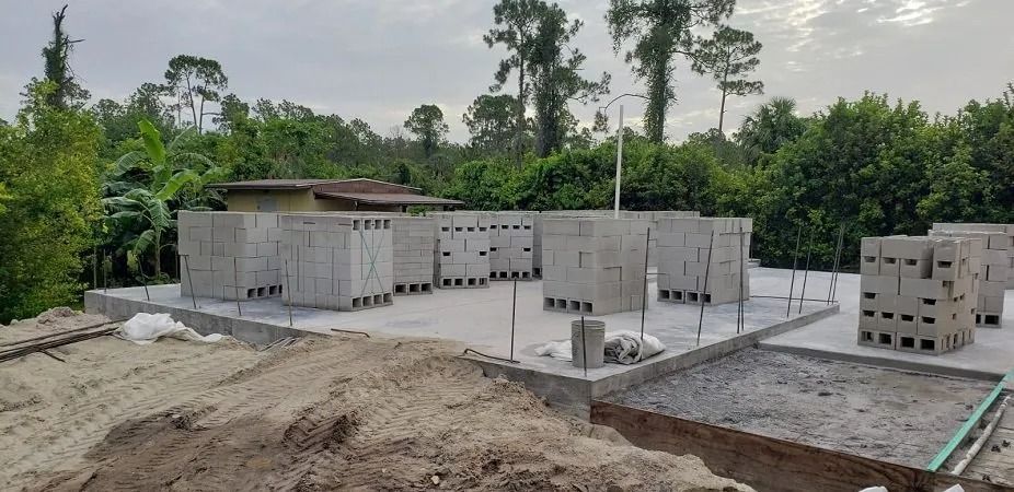 Construction site: concrete block walls partially built. Exterior with trees in the background.