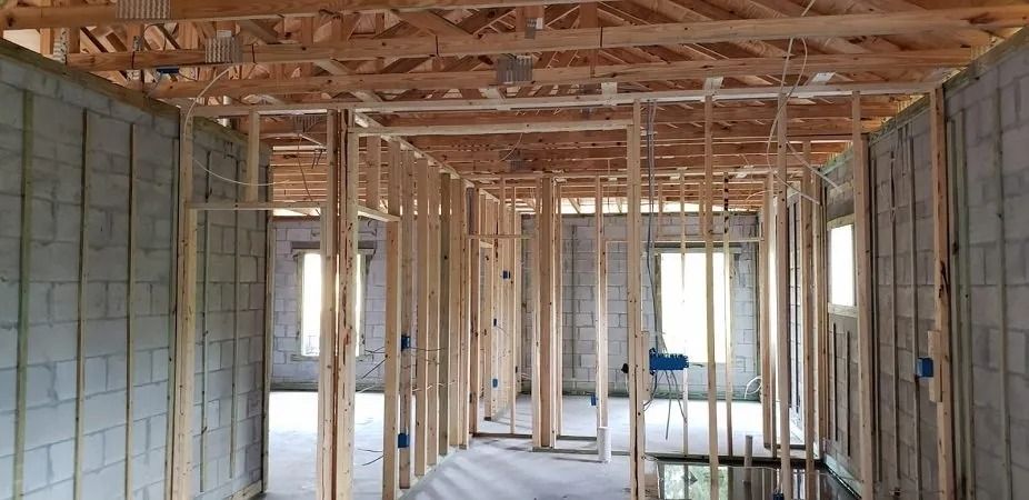 Interior view of a building under construction. Wood framing is installed on the walls and ceiling.