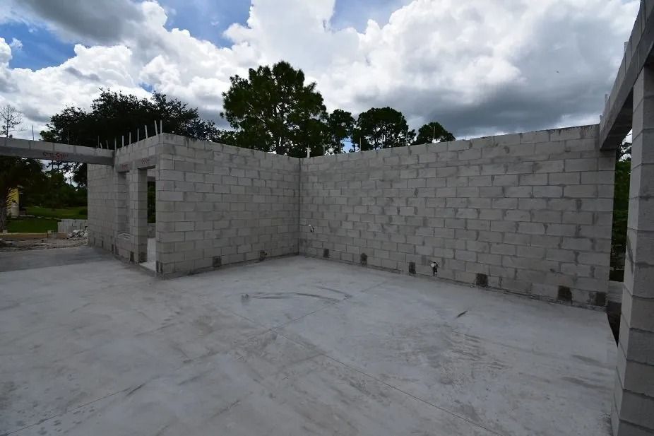 Concrete block building under construction; interior view with gray walls and floor, cloudy sky background.
