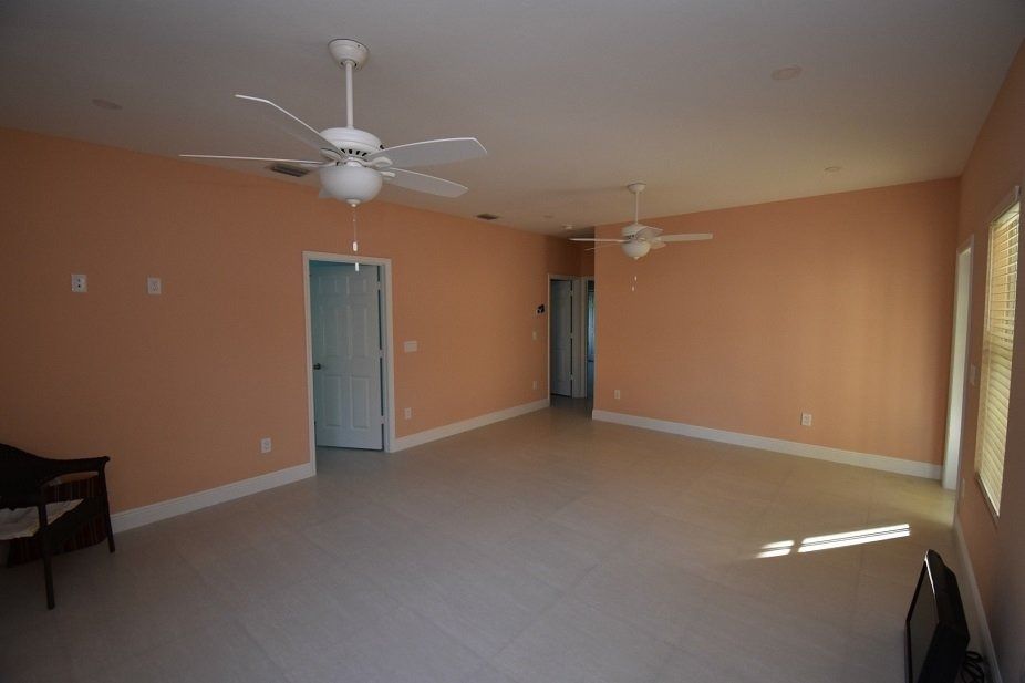 Empty room with peach walls, white trim, two ceiling fans, and tile floor.