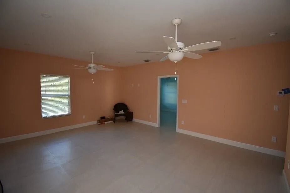 Empty room with peach walls, white tile floor, and two ceiling fans.