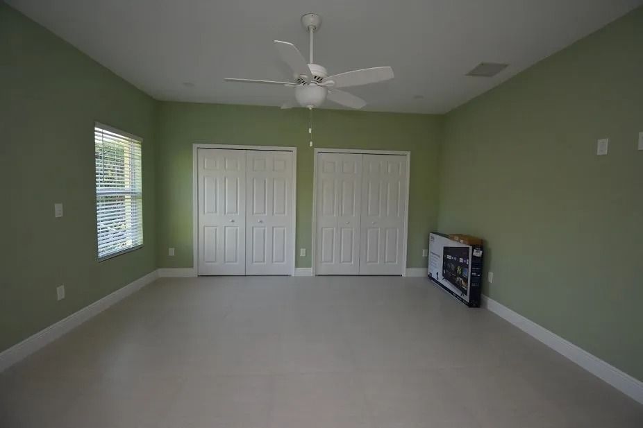 Empty room with light green walls, white doors and trim, ceiling fan, and beige floor.