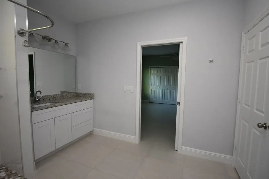 Bathroom with white cabinets, gray walls, and a doorway to a closet.