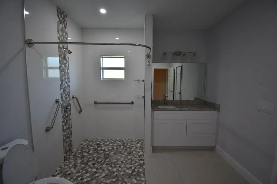 Accessible bathroom with a roll-in shower, grab bars, and a low-threshold toilet. Light gray walls and white vanity.
